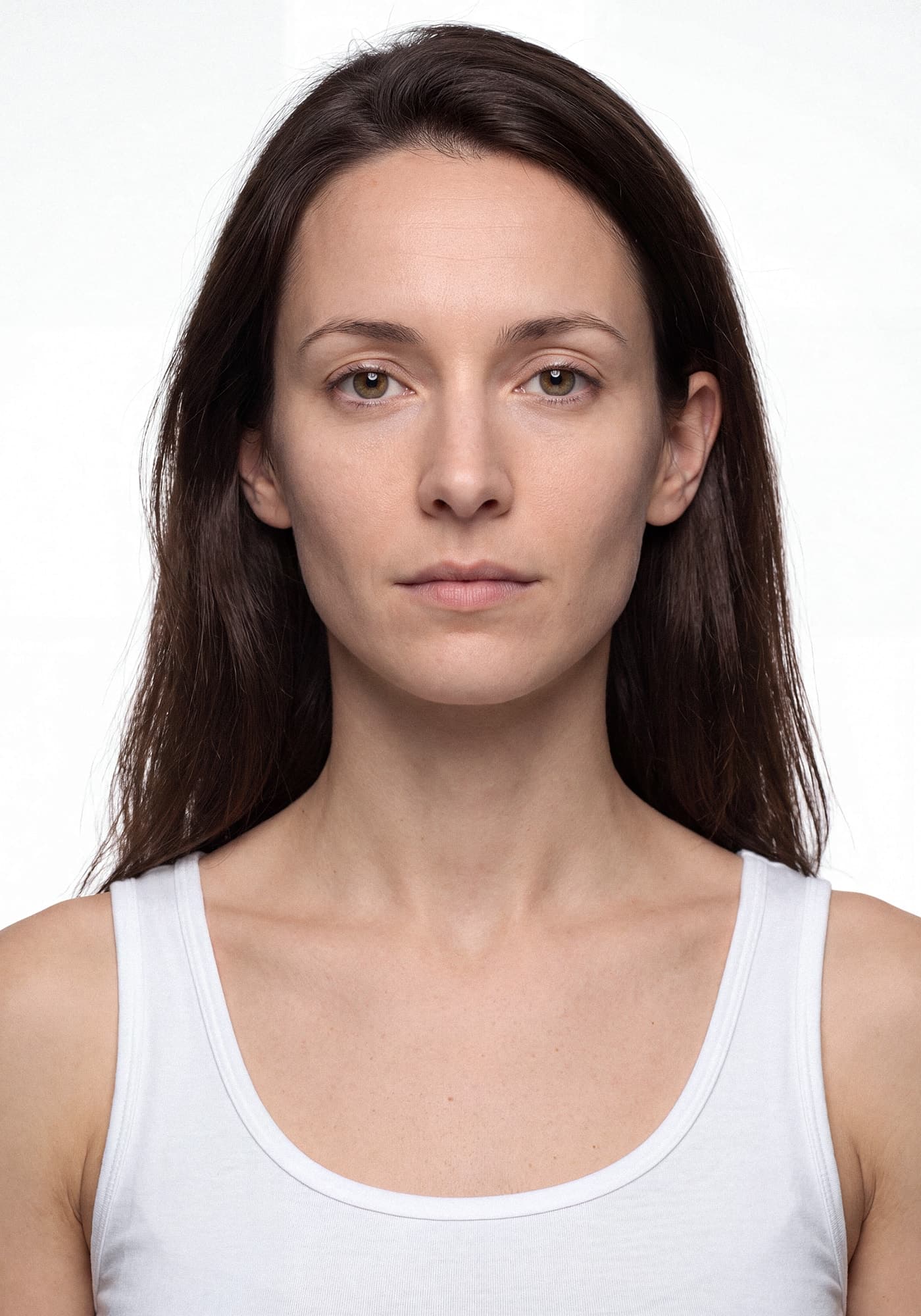 Portrait de face de la mannequin de référence, cheveux bruns détachés, débardeur blanc, sur fond clair.